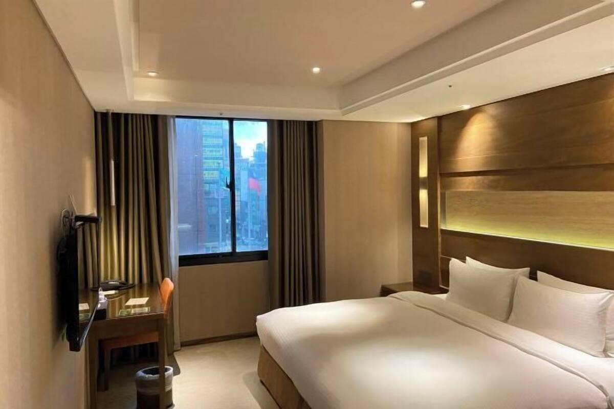 A hotel room with a large bed, a desk with a chair, a TV, and a window with curtains.