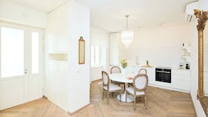 A spacious dining area with a round table and chairs, a chandelier, and a kitchen area with white cabinets and a stove. - Hedera Estate, Hedera A8 (Dubrovnik)