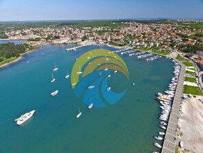 An aerial view of a coastal town with a marina, boats, and a large green area with a distinctive logo. - Holiday apartment with air conditioning (Medulin)