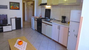 A compact kitchen with a stove, sink, and refrigerator. There is a small dining area with a table and a single orange on a doily. - Holiday apartment with air conditioning (Medulin)