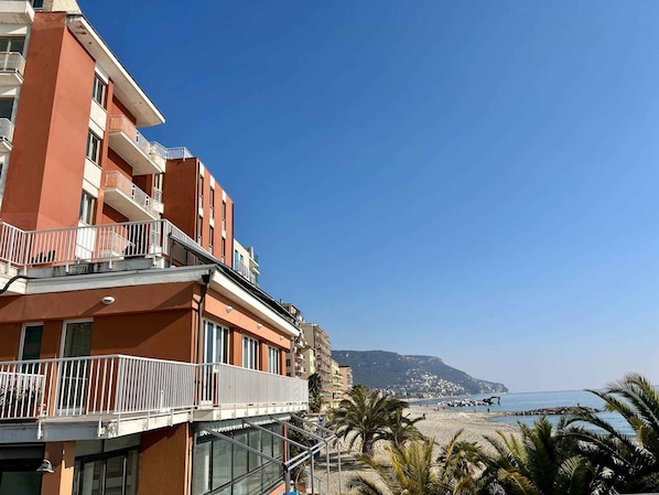 A multi-story building with balconies, a beach view, and a clear sky.