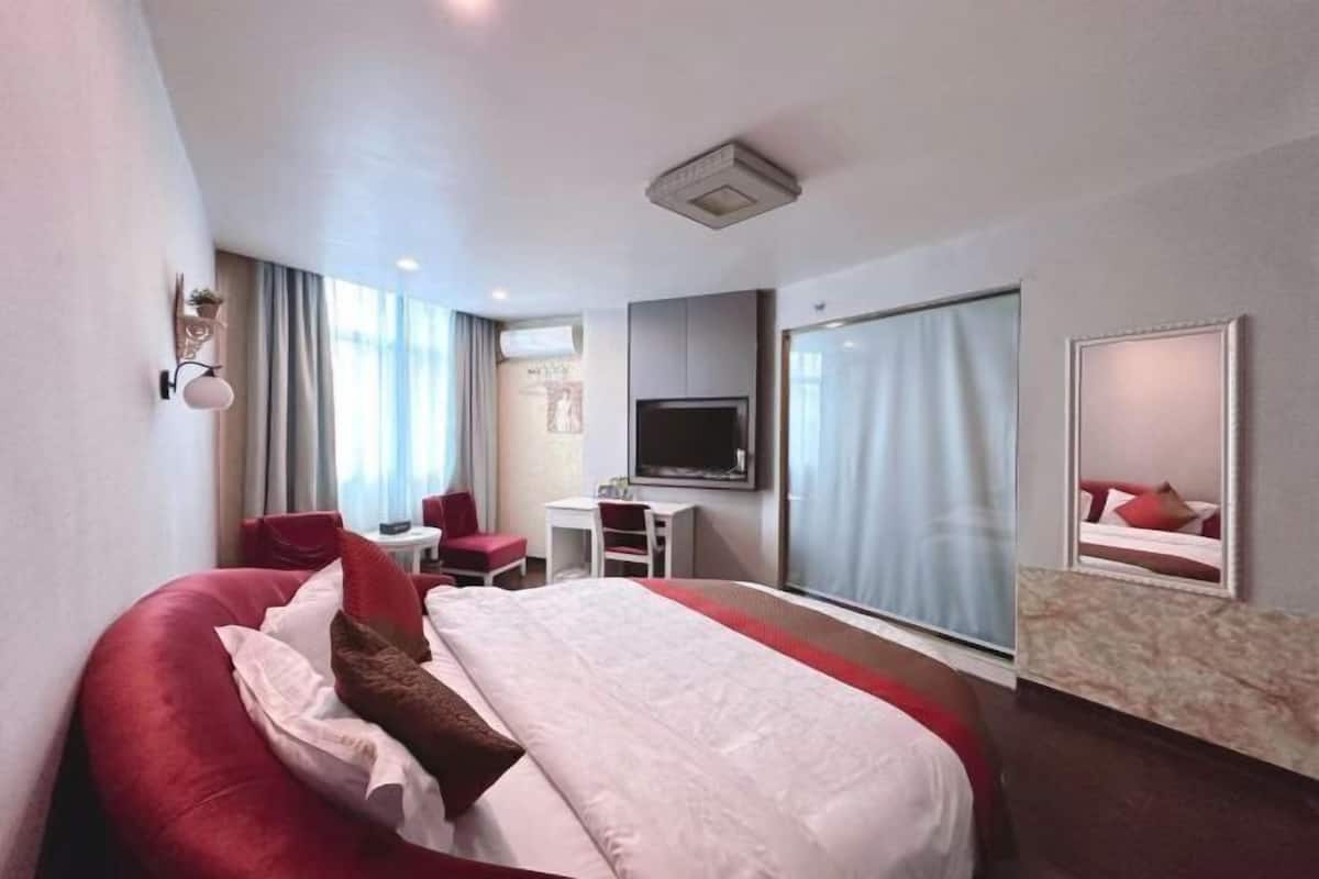A hotel room with a large bed, a desk, a chair, a TV, and a large window.