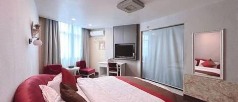 A hotel room with a large bed, a desk, a chair, a TV, and a large window.