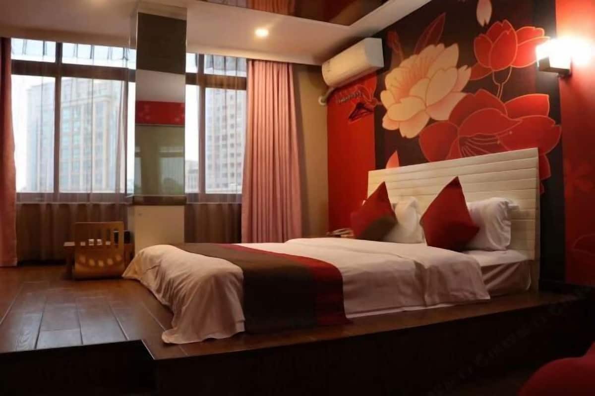 A hotel room with a large bed, a wooden floor, a window with curtains, and a floral wall mural.