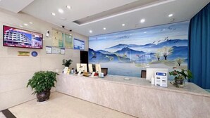 Zona de recepción con pantalla digital, un cuadro de montañas y agua, y un mostrador con una planta.