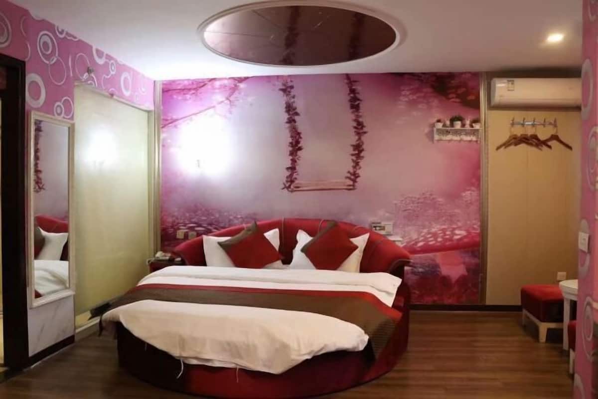 A circular bed with red and white bedding, a mirror, a wall with a floral pattern, and a hanging plant.