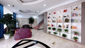 Un lobby moderno con un sofá púrpura, una estantería blanca con plantas y una escalera.
