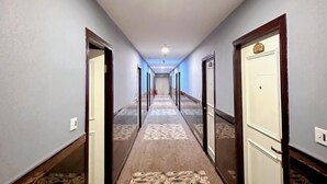 Un largo y estrecho pasillo de hotel con alfombra estampada, puertas de madera y pared de color claro.