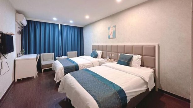 Habitación de hotel con dos camas, un escritorio, una silla, un televisor y un cuadro en la pared.