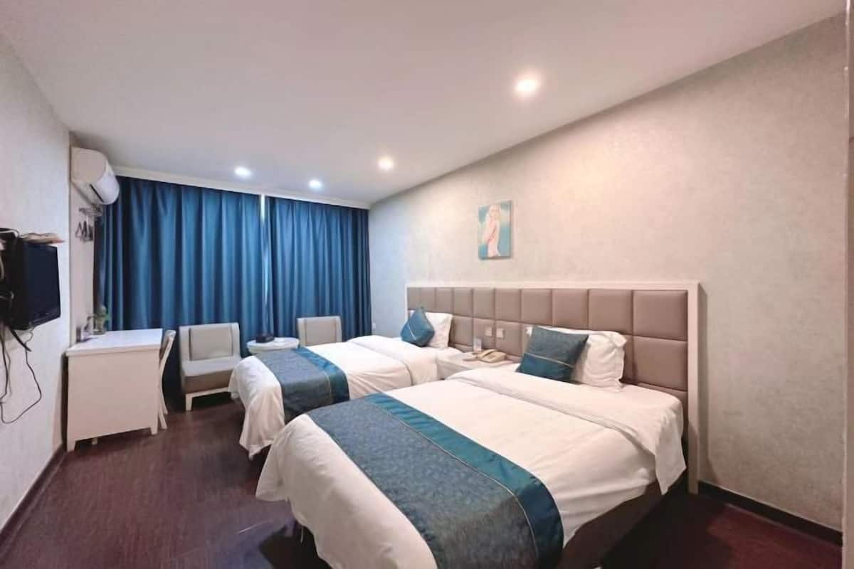 A hotel room with two beds, a desk, a chair, a television, and a painting on the wall.