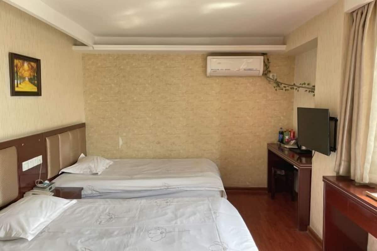 A hotel room with two beds, a desk with a television, and a wall-mounted air conditioner.