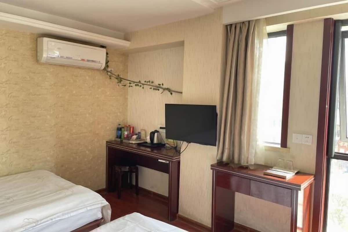 A hotel room with a bed, a desk with a television, a small table, and a window with curtains.