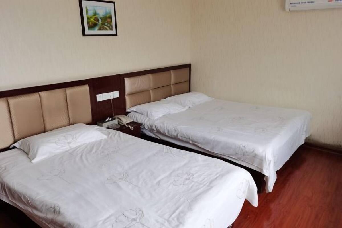 A hotel room with two single beds, a wooden headboard, a bedside telephone, and a framed picture on the wall.