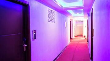A hotel corridor with a red carpet, a QR code on the wall, and a door on the left.