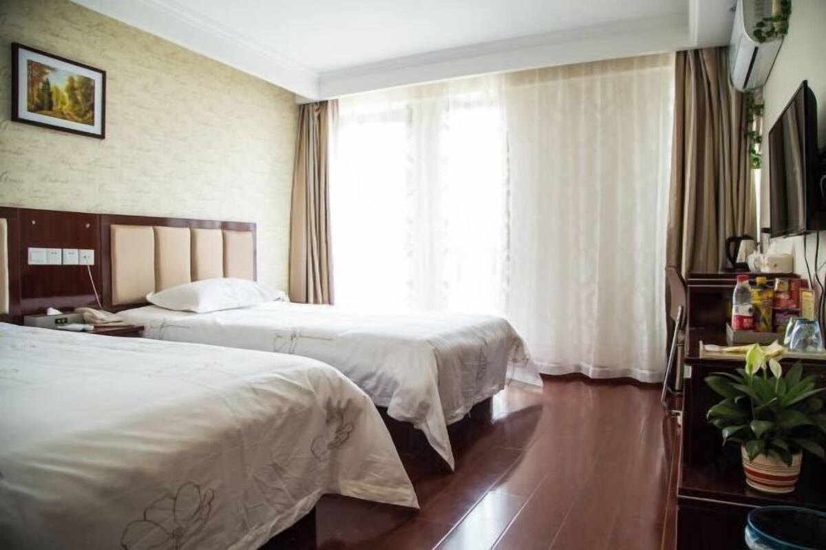 A hotel room with two beds, a TV, a desk with a plant, and a window with curtains.