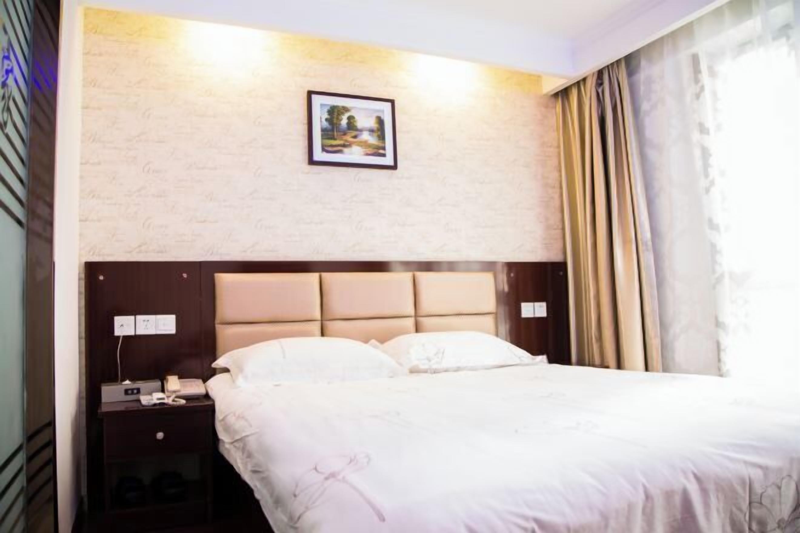 Hotellihuone, jossa on sänky, yöpöytä, jossa on puhelin, seinälle ripustettu taulu ja ikkuna, jossa on verhot.