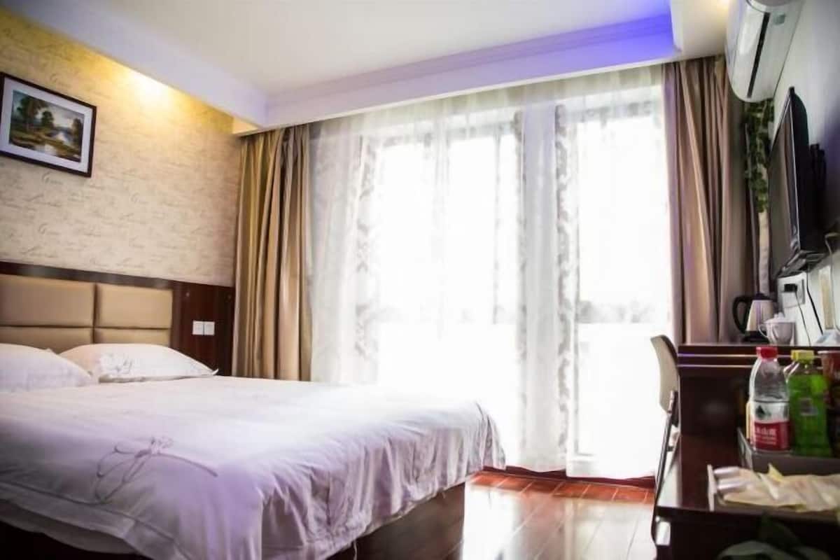 A hotel room with a bed, a desk, a chair, a TV, and a window with curtains.