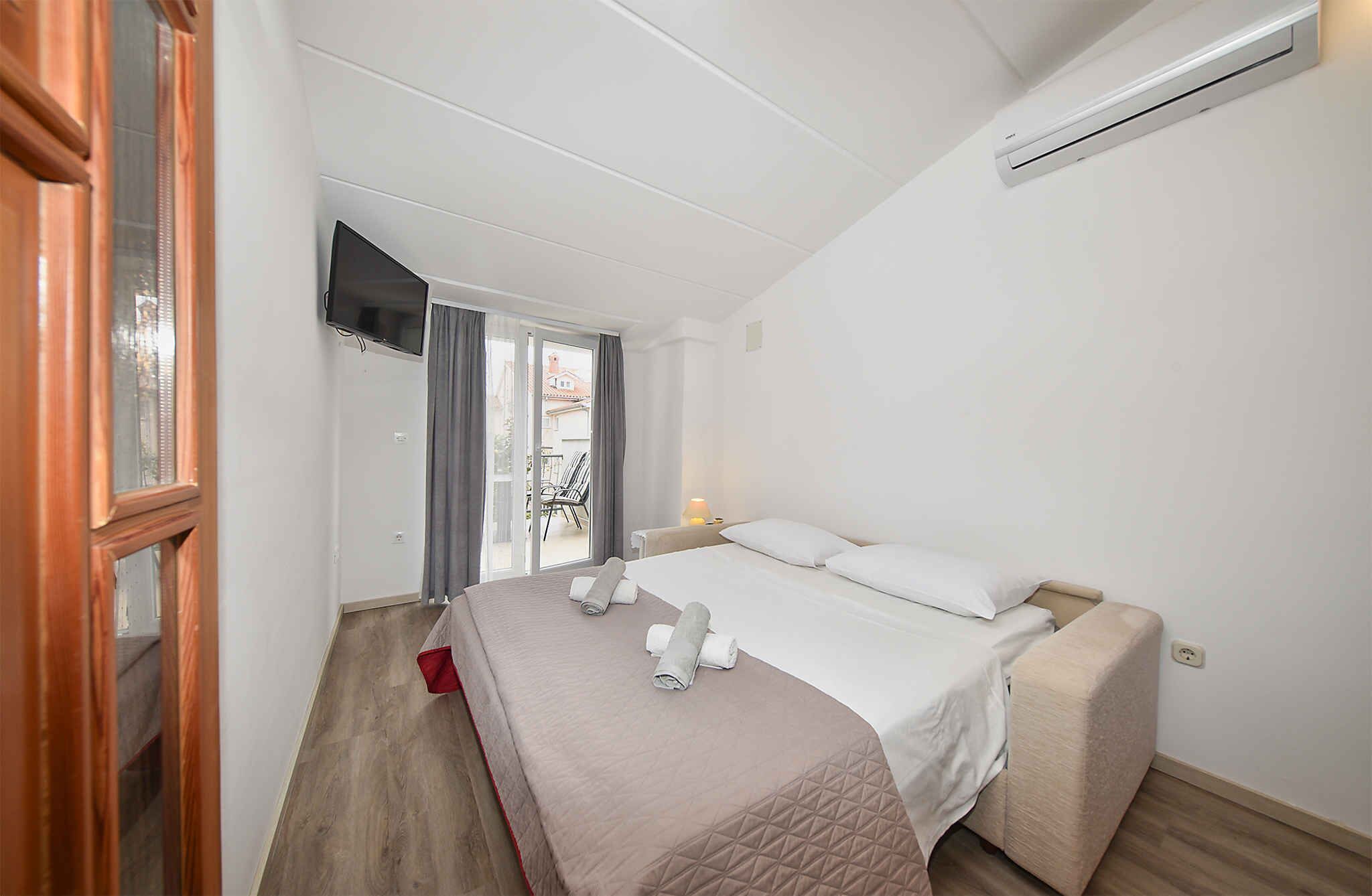 Quarto com cama, televisão, ar condicionado e porta de correr para uma varanda.