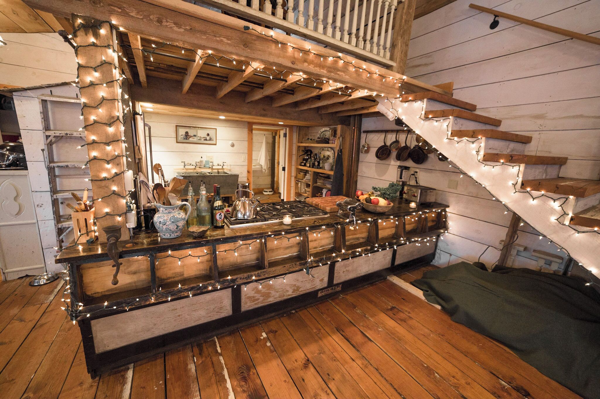 A rustic kitchen with wooden beams, a wooden staircase, and string lights.