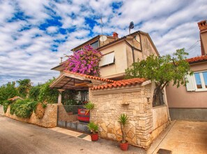 A two-story house with a stone facade, a red-tiled roof, and a small garden with potted plants. - Holiday apartment with air conditioning (Medulin)