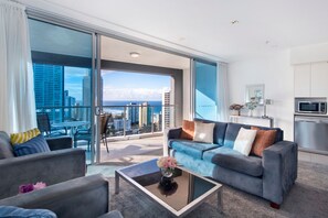 A modern living room with a sofa, chairs, a coffee table, and a view of the city and ocean.