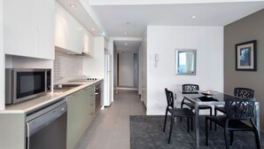 A modern kitchen with stainless steel appliances, a dining area with a table and chairs, and a view of the outdoors through a window.