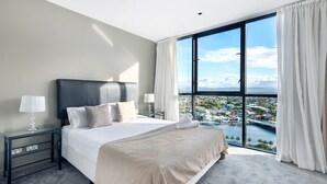 A modern hotel room with a large bed, two bedside tables, and a view of a cityscape through floor-to-ceiling windows.