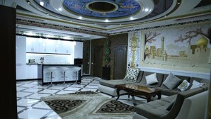 Un'ampia zona giorno con divano, tavolino e un tappeto decorato. Sullo sfondo, si intravede una cucina con mobili bianchi e una zona pranzo con uno sgabello da bar.