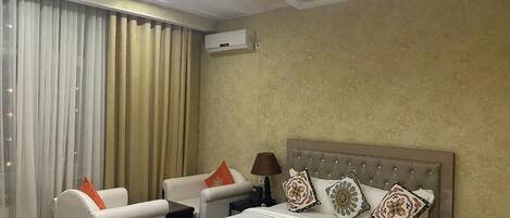 A hotel room with a bed, two armchairs, a nightstand, and a lamp.