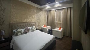 Una camera d'albergo con un letto grande, due poltrone bianche, una TV e una lampada a soffitto.
