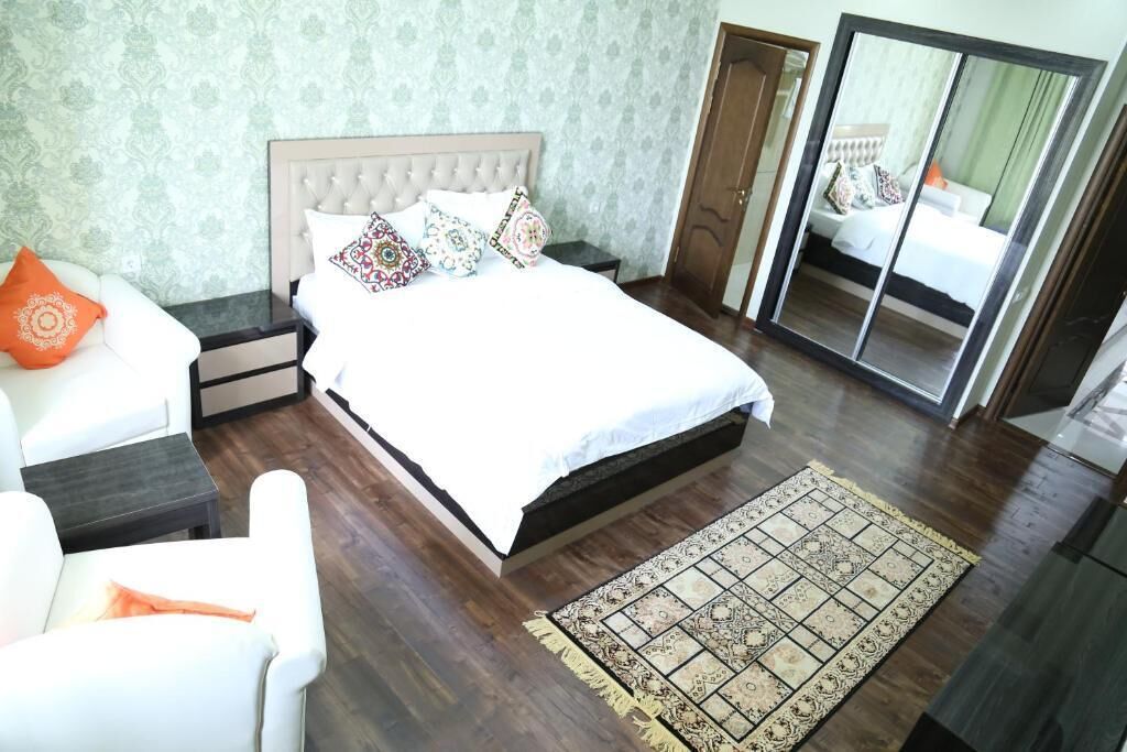 Quarto com uma cama grande, mesa de cabeceira, cadeira, espelho e tapete estampado.