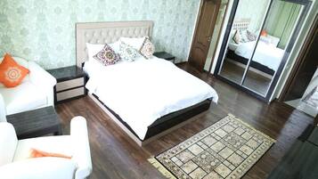 Quarto com uma cama grande, mesa de cabeceira, cadeira, espelho e tapete estampado.