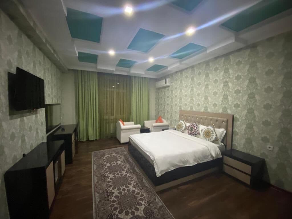 A bedroom with a bed, bedside tables, a TV, and a patterned rug.