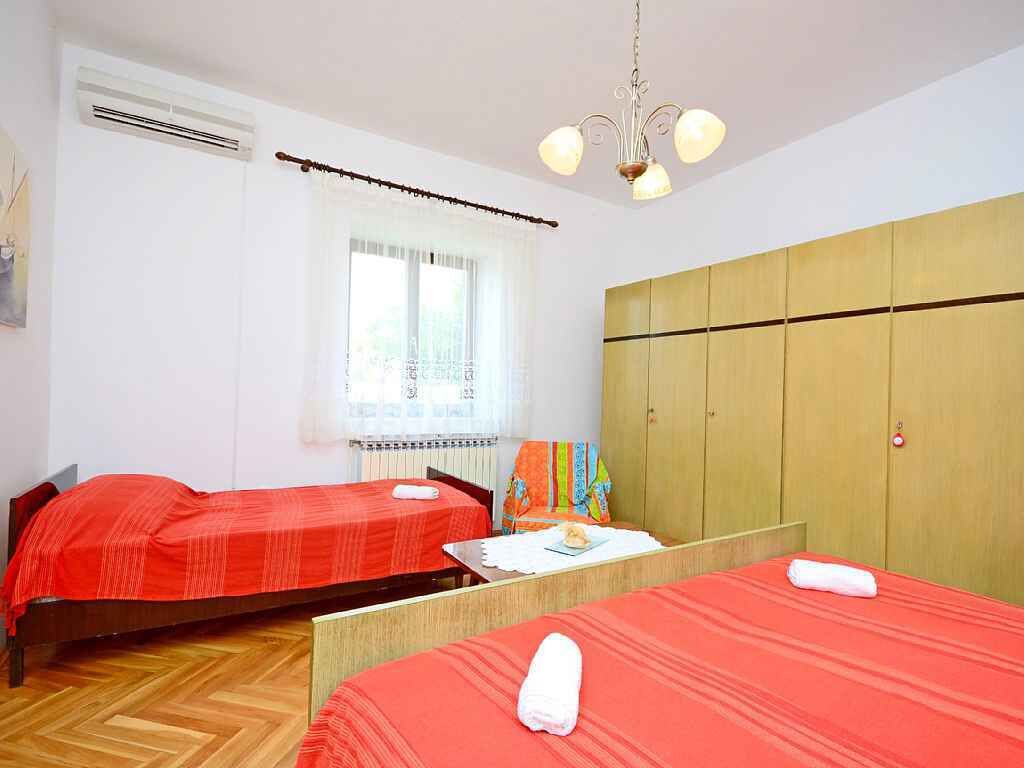 Une chambre avec deux lits, une armoire en bois, une fenêtre avec des rideaux et un luminaire au plafond.