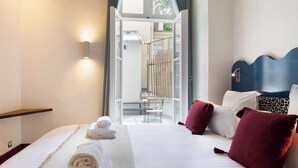 Habitación de hotel con cama, almohadas, mesita de noche y vistas al balcón exterior.