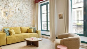 Una sala de estar con pared de piedra, un sofá amarillo, una mesa de centro redonda y un sillón color crema.