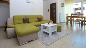 A modern living room with a green sofa, a white coffee table, and a dining area with wooden chairs and a table. - Holiday home with air conditioning (Peroj)