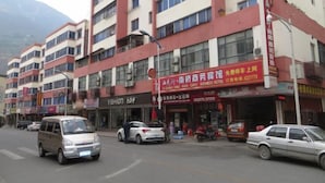 Un hotel de varios pisos con fachada roja y blanca, varias tiendas en la planta baja y montañas al fondo.