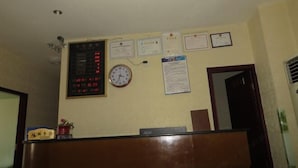 Zona de recepción con pantalla digital, reloj y varios certificados en la pared.