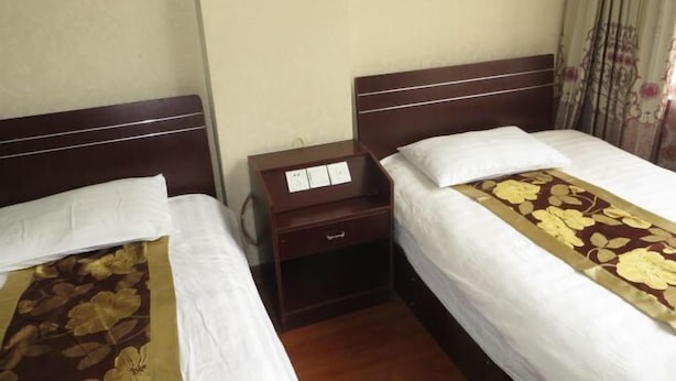 Una habitación de hotel con dos camas individuales, una mesita de noche de madera con cajón y una colcha estampada con motivos florales.
