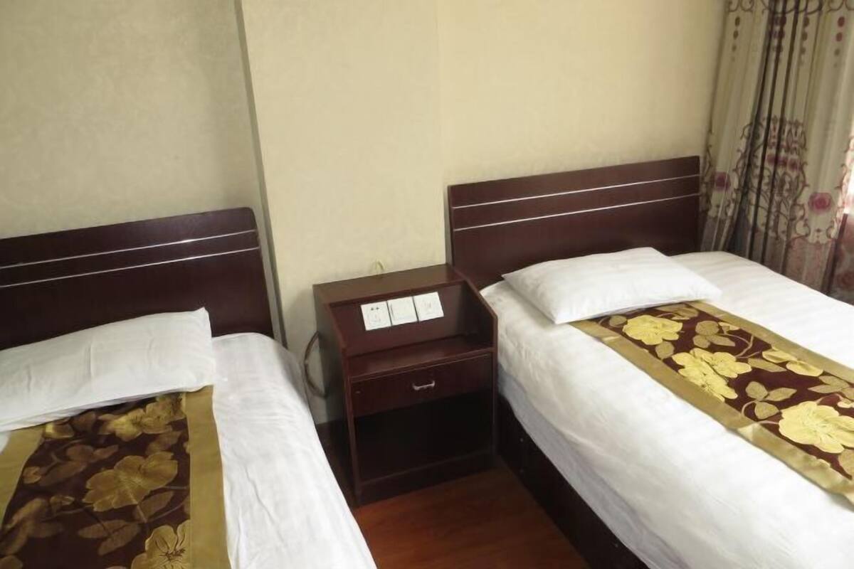 A hotel room with two single beds, a wooden nightstand with a drawer, and a floral bedspread.