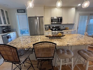 Una cocina con armarios blancos, electrodomésticos de acero inoxidable, encimera de granito y una isla central con taburetes.