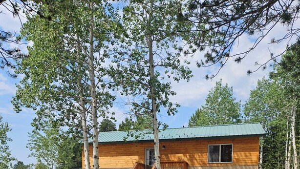 Une cabane avec une façade en bois, une véranda et un espace barbecue avec des chaises Adirondack.