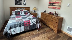 Une chambre avec un grand lit, un ventilateur de plafond, une commode en bois et des œuvres d’art murales.