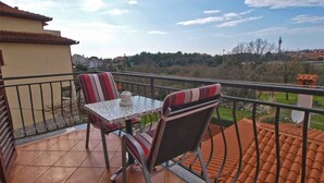 Un balcon avec une table et deux chaises, un sol carrelé et une vue sur la campagne.