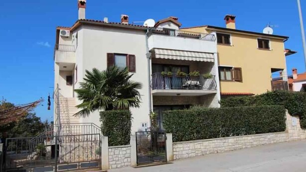 Un immeuble résidentiel à deux étages, doté d’un balcon, d’une grille et d’une haie bien entretenue.