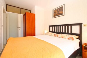 A bedroom with a bed, a wardrobe, a nightstand, and a painting on the wall. - Holiday apartment with barbecue (Pješćana Uvala)