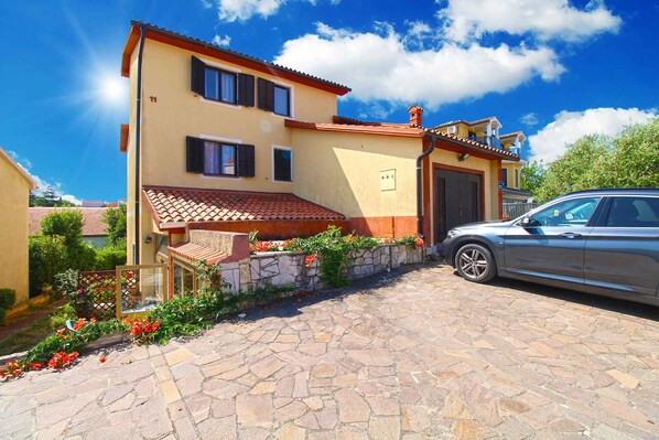 A two-story house with a stone-paved driveway and a parked car. - Holiday apartment with barbecue (Pješćana Uvala)
