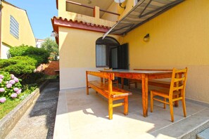 An outdoor patio with a wooden table and chairs, a tiled floor, and a yellow building in the background. - Holiday apartment with barbecue (Pješćana Uvala)