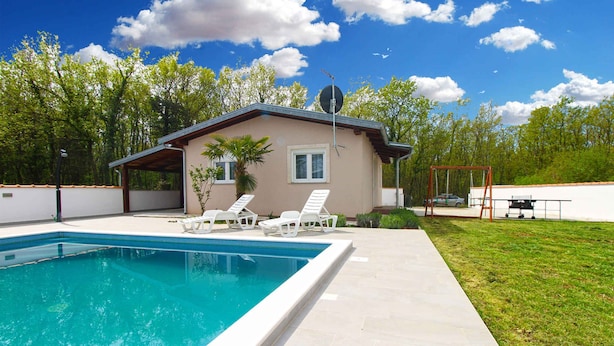 Una piscina con sillas de descanso, una casa pequeña con antena parabólica y un columpio.